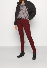 Chaqueta de plumas negra, blusa gris de estampado y vaqueros ajustados burdeos. Botines negros completan el atuendo.