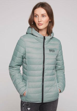 Light green puffer jacket with hood, featuring horizontal quilted design, black zipper, and a logo. Side pockets on both sides.