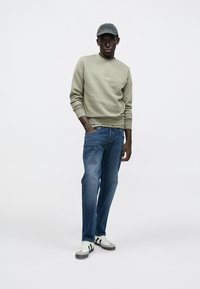 Felpa verde oliva, jeans di denim blu, berretto grigio e sneakers bianche con strisce nere. Vestibilità casual, tessuto leggero e design semplice.