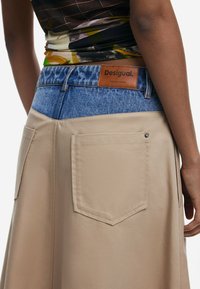 Jupe beige avec une taille en denim et deux poches arrière, en tissu texturé avec un design en blocs de couleur contrastants. Accent en cuir avec logo.