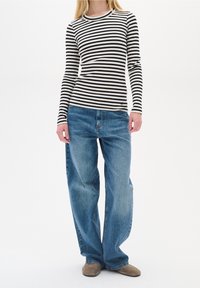 Top a maniche lunghe a righe bianche e nere con trama a coste, abbinato a jeans azzurri dalla vestibilità ampia, caratterizzati da un taglio dritto e una texture scolorita.