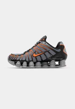Baskets de sport grises avec des accents orange, empeigne en mesh texturé, design distinctif en forme de vague et semelle rembourrée notable pour un meilleur soutien.