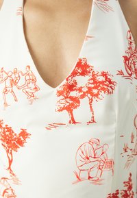 Balta maudymosi kostiumėlis su gilia iškirpte, papuoštas raudonais piešiniais, vaizduojančiais žmones, medžius ir peizažus, pasižymi lygiu audiniu ir prigludusia forma.