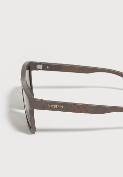 Καφέ ορθογώνια γυαλιά ηλίου Burberry με διακριτικό καρό σχέδιο και χρυσό λογότυπο στο μπράτσο, εμφανίζονται σε λευκό φόντο.