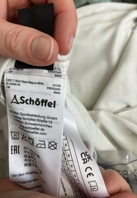 White fabric care label with black text detailing washing instructions, size, and brand "Schöffel." Includes EAC symbol and care icons.