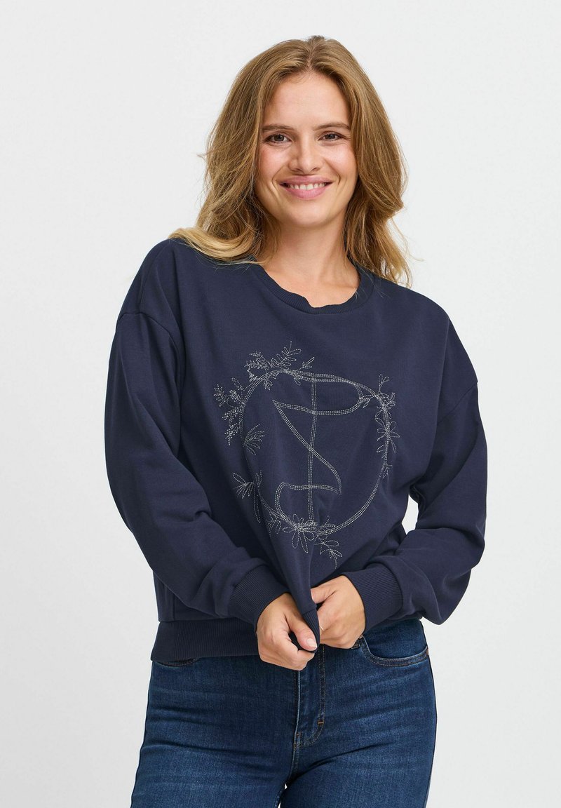 Sudadera navy con un corte relajado, que presenta un logo con un patrón floral en bordado plateado. Tejido suave y puños acanalados en el dobladillo.
