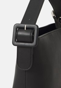 Borsa a tracolla in pelle nera con una tracolla piatta che presenta una fibbia quadrata e dettagli di cucitura. L'apertura superiore con cerniera rivela uno spazio interno.