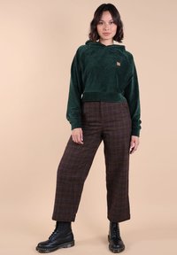 Haut à capuche court en velours côtelé vert avec un logo sur le devant, associé à un pantalon large en tartan marron et des bottes noires à lacets.