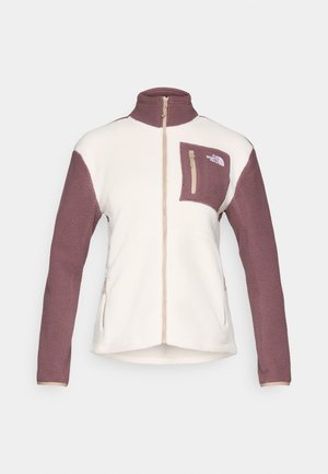 Chaqueta de forro polar en crema con mangas burdeos. Presenta un bolsillo en el pecho con cremallera y un cuello alto. Textura suave con un cierre de cremallera completa.