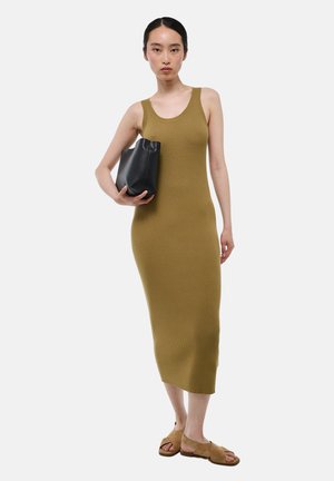 Robe midi en maille côtelée vert olive avec un décolleté arrondi, associée à un sac noir. Le modèle porte des sandales à glisser marron.