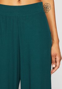 Pantalons larges en teal en tissu côtelé. Comprend une taille élastique et une texture verticale pour un ajustement doux et confortable.