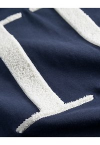 Tejido de algodón azul marino con un diseño texturado de toalla blanca. Presenta letras blancas gruesas y suaves integradas en el material.