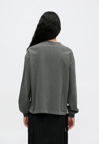 Szary oversize sweatshirt z długimi rękawami, okrągłym dekoltem, miękką teksturą materiału i surowymi detalami przy hemie, stylizowany z czarną spódnicą.