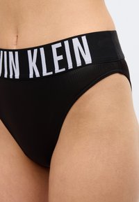 Κοντινό πλάνο ενός ατόμου που φορά μαύρα εσώρουχα Calvin Klein με φαρδιά ελαστική μέση που φέρει το όνομα της μάρκας σε λευκά γράμματα.