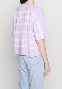 Violetti t-paita, jossa on lyhyet hihat, pyöreä kaula-aukko ja lyhennetty malli. Siinä on vaakasuoria valkoisia raitoja, jotka antavat tekstuuria.