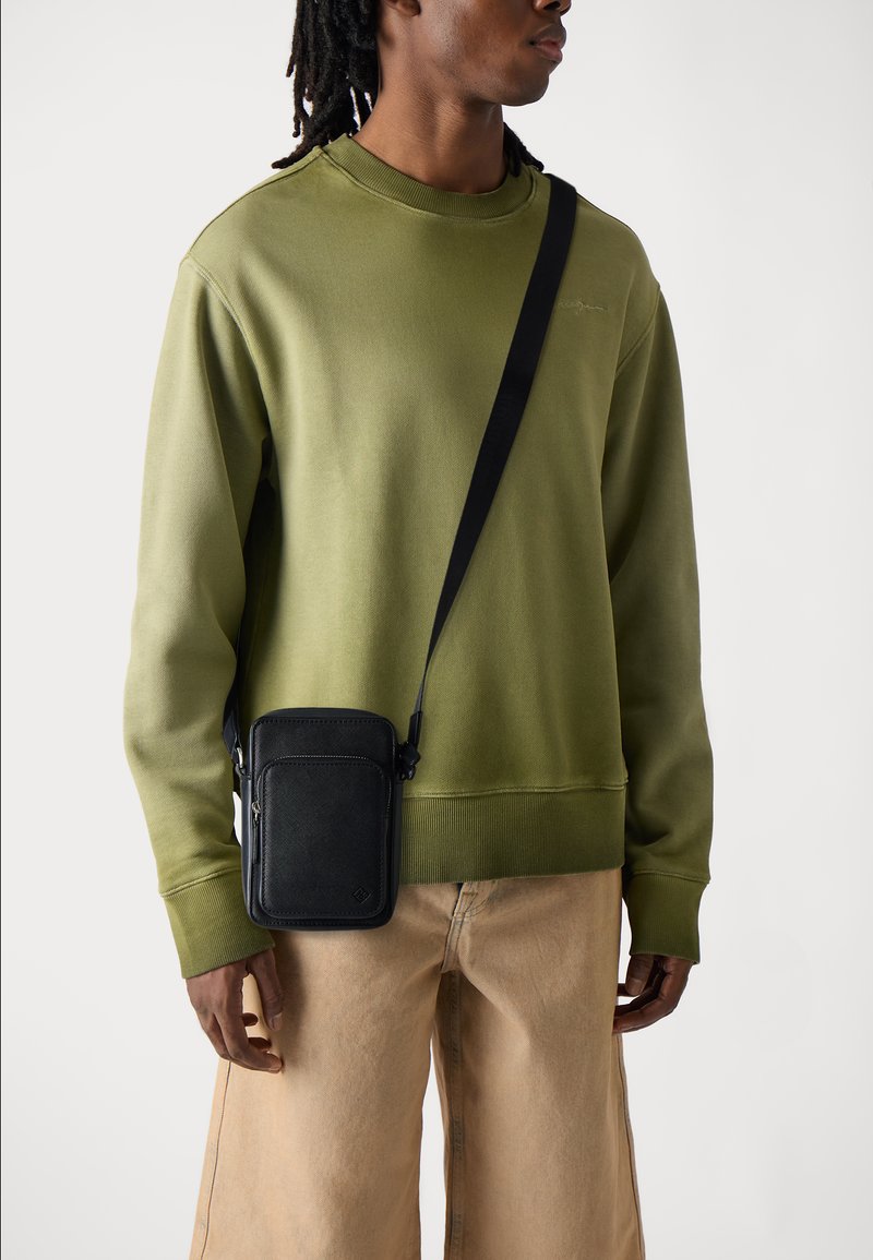 Oliven Grøn sweatshirt med rund hals, kombineret med beige vidde bukser. Sort crossbody taske med tekstureret overflade og lynlåsdetalje.