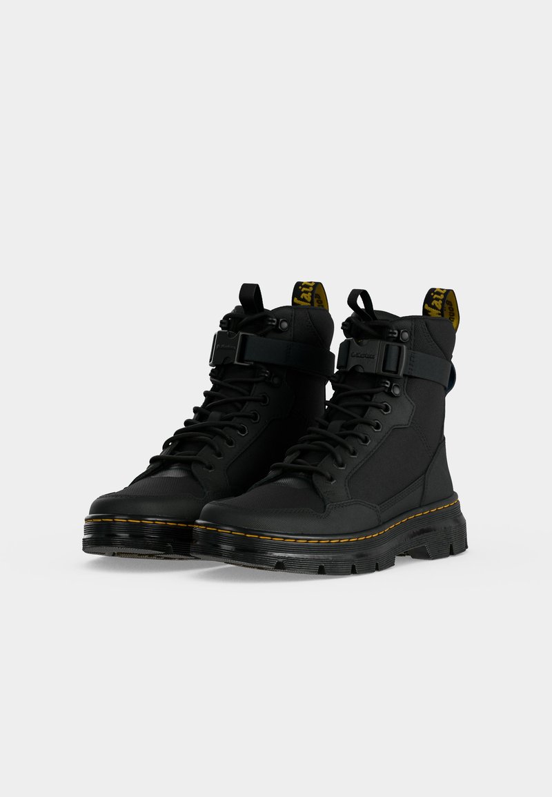 Pair of black lace-up combat boots with yellow stitching and buckle straps on a white background.