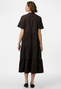 Brūns daudzslāņu kleita ar īsām piedurknēm, kas ar saplacinātu krūšu daļu un frillētu apakšmalu. Audums šķiet gluds un viegls.