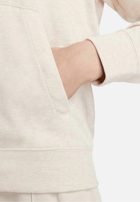 Ljus beige sweatshirt med en känguru ficka och ribbad mudd, tillverkad av mjukt tyg som visar en slät textur och sömlös design.