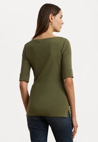Olijfgroen, getailleerd langshirt met opgerolde mouwen; heeft een brede halslijn en zijsplitten aan de zoom voor extra ontwerpelementen.
