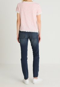 Roze en witte gestreepte t-shirt met kantafwerking, gecombineerd met donkerblauwe jeans en witte sneakers. Het t-shirt heeft een zachte stof en een relaxte pasvorm.