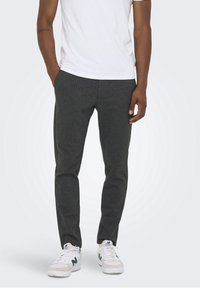 Pantalons à rayures gris foncé, coupe slim, en tissu. Portés avec un t-shirt blanc et des baskets blanches avec des accents verts.