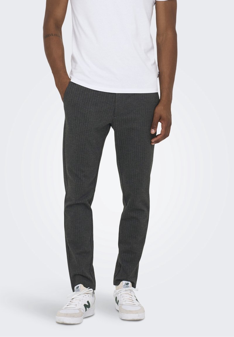 Pantalons à rayures gris foncé, coupe slim, en tissu. Portés avec un t-shirt blanc et des baskets blanches avec des accents verts.