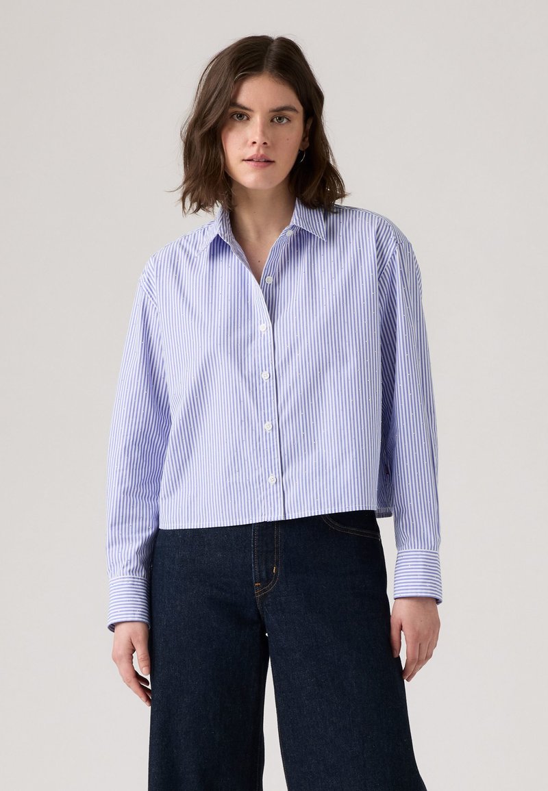 Chemise courte à rayures bleues et blanches, à boutons, avec col écarté et manches longues. Fini avec une texture de tissu lisse et propre.