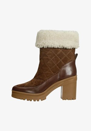 Stivale alla caviglia in suede marrone con un morbido risvolto in pelliccia crema, texture trapuntata e un tacco chunky marrone. Presenta una suola in gomma per una migliore aderenza.
