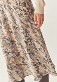 En knælang kjole med slangeskinds mønster i beige, sort og grå nuancer. Den bløde tekstur hænger flydende med en let udskåret søm.