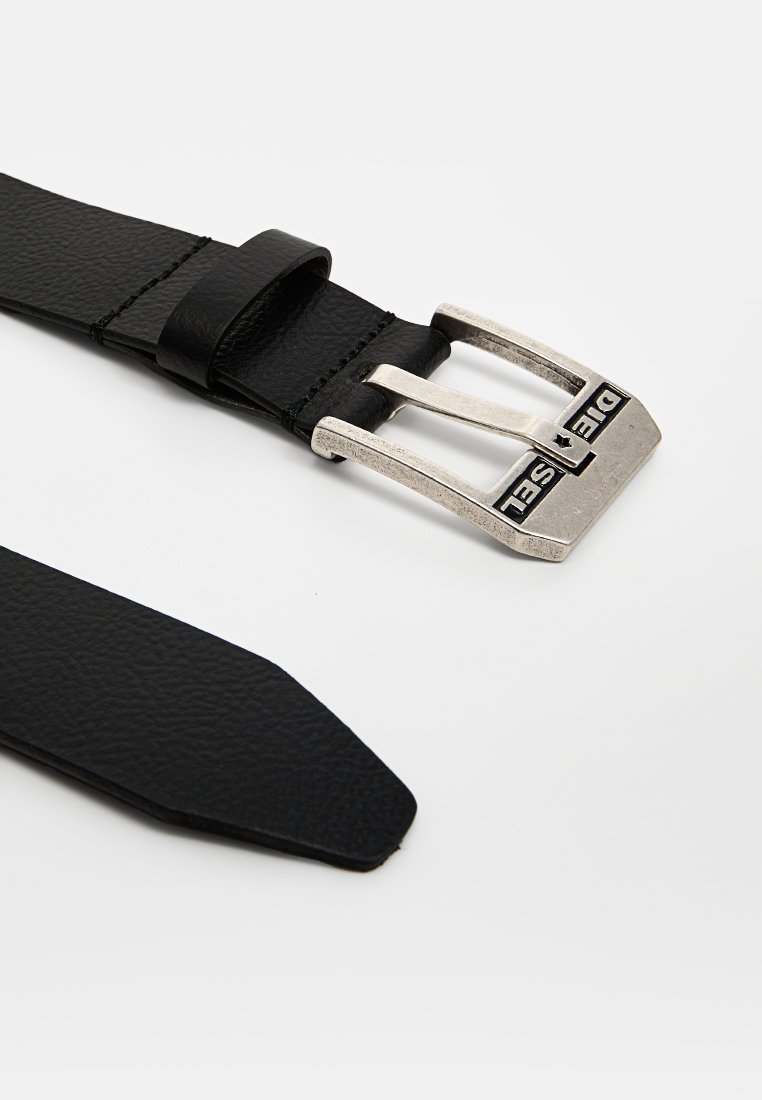 Ceinture en cuir noir avec une boucle en métal argenté rectangulaire gravée du logo, sangle texturée et extrémité effilée pour un maintien sécurisé.