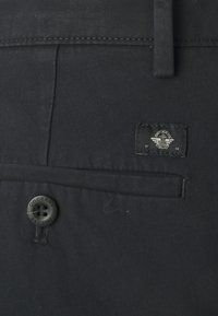 Svarta tygbyxor med en bakficka, knäppning med knapp och en etikett med en stiliserad logotyp. Materialet verkar slätt och hållbart.