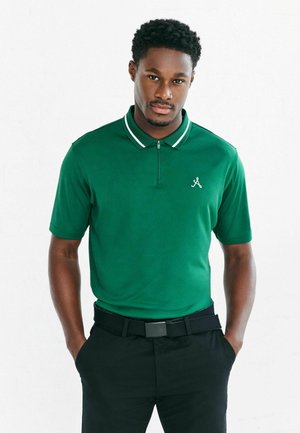 Grön pikétröja med vita ränder på kragen, korta ärmar och en dragkedja framtill. Har en liten logotyp på vänster bröst. Bärs med svarta byxor.