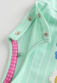Nærbillede af mintgrønne babyklæder med sølvfarvede trykknapper og lyserødt ginghambånd inde i halsudskæringen.