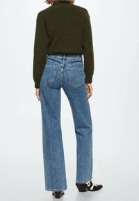 Jeans de mezclilla azul de cintura alta con piernas anchas, que cuentan con dos bolsillos traseros y costuras en contraste, combinados con un suéter de punto verde oliva.