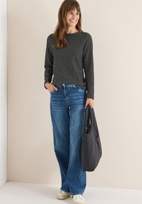 Maglietta a maniche lunghe nera e bianca con texture, jeans larghi blu, sneakers bianche, in mano una borsa imbottita nera. Outfit semplice e casual.