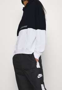 Hoodie i svart och vitt, med en sportig design, ficka med blixtlås och logotext. Kombineras med svarta byxor med vita detaljer.