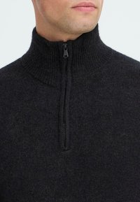 Zwarte sweater met hoge hals en een gestructureerde brei-afwerking, met een halve rits aan de voorkant voor een verstelbare sluiting. Zachte wolmix.