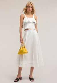 Top corto bianco con bordo arricciato nero, gonna midi bianca, borsa gialla, sandali neri a infradito, tessuto liscio e trame morbide.