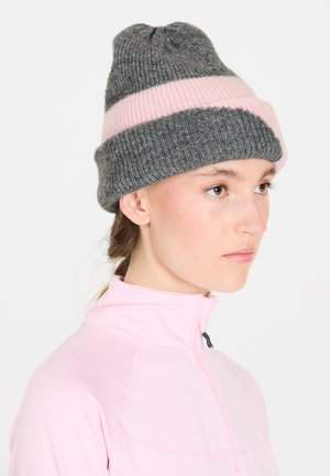 Grå stickad mössa med en rosa horisontell rand, med ribbat mönster och en avsmalnande topp. Bärs tillsammans med en rosa zip-up-topp.
