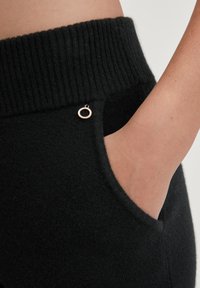 Zwarte geribbelde tailleband met een gladde stofstructuur; voorzien van een zijzak en een klein ronde hardware detail.