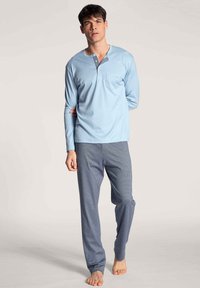 Lichtblauw langemouwen pyjama top met een henley halslijn en knoopdetails; gecombineerd met donkerblauwe geruite broek, gemaakt van zacht materiaal.
