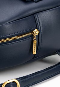 Granatowa skórzana torebka na ramię z złotym zamkiem błyskawicznym, okuciami i metką z logo. Powierzchnia jest gładka z delikatnymi detalami szycia.