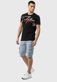 T-shirt en coton noir avec imprimé graphique rouge et blanc, associé à un short cargo à rayures bleu clair. Agrémenté de poches et de baskets blanches.