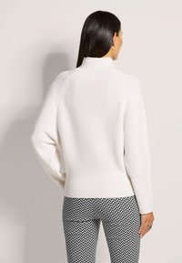 Weißer Pullover mit strukturiertem Strickmuster, Stehkragen und geripptem Saum. Kombiniert mit Leggings im schwarz-weißen Karomuster.