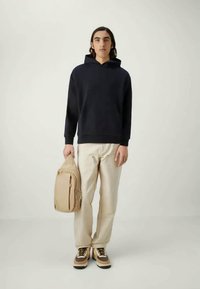 Ναυτικό φούτερ, μπεζ σακίδιο, ανοιχτόχρωμο παντελόνι και καφέ αθλητικά παπούτσια. Η υφή φαίνεται απαλή, τα υλικά φαίνονται ανθεκτικά, με μινιμαλιστικό σχέδιο.