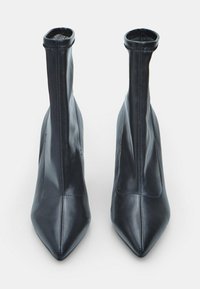 Botines de cuero negro hasta el tobillo con punta afilada, diseño estilizado y detalle de cuello acanalado. Textura suave con acentos de costura mínimos.