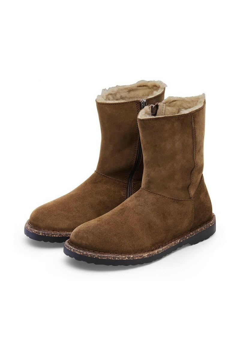 Bottines en suède marron avec une fermeture éclair, doublure en fourrure douce, semelle en caoutchouc plate et détails cousus sur le bord de la semelle.