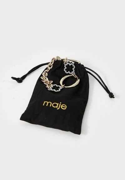 Bracciale in metallo dorato e argentato con accenti floreali, adagiato su un sacchetto di velluto nero con il logo dorato "maje".