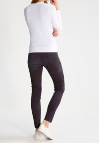 Bílý bezrukávový top, přiléhavý střih, s kulatým výstřihem; v kombinaci s tmavými slim-fit kalhotami a bílými teniskami. Celkově hladká textura.